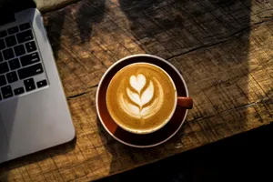 caffe latte on white ceramic cup beside silver and black laptop computer jigsaw puzzle