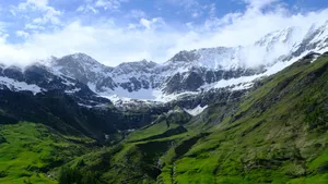Stunning aerial view of snowcapped mountains and lush green valley under a clear blue sky. jigsaw puzzle