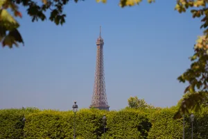 Scenic view of the Eiffel Tower framed by lush green trees against a clear blue sky in Paris, France. jigsaw puzzle