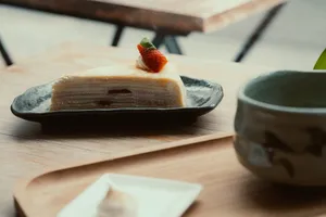 A slice of crepe cake topped with a strawberry, served on a wooden table. jigsaw puzzle