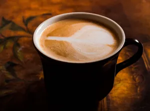A close-up of a cappuccino in a black mug with latte art, against a warm, artistic background. jigsaw puzzle