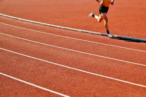 Athlete running on a red track in an outdoor stadium on a sunny day. jigsaw puzzle