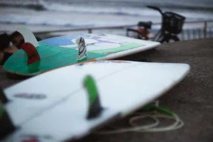 Close-up of surfboards on a beachside with waves and bicycle in the background. jigsaw puzzle