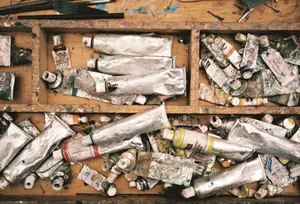 A top-down view of a cluttered artist's workspace filled with used paint tubes and brushes. jigsaw puzzle