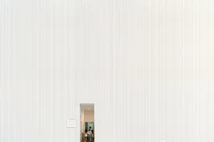 A large white textured wall with a small doorway entrance and visible people inside. jigsaw puzzle
