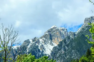 Snow-capped mountains under a cloudy sky with green trees. jigsaw puzzle