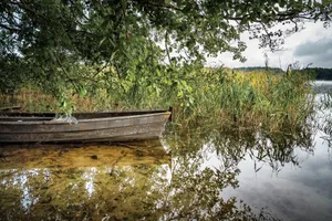 A serene lakeside view with a rustic boat under lush greenery, reflecting natural beauty. jigsaw puzzle