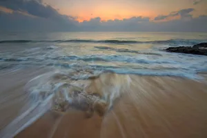 Long exposure capture of ocean waves washing onto a sandy beach during a serene sunrise. jigsaw puzzle