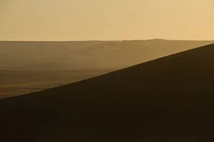 Capture the tranquility of a barren desert landscape with rolling hills at sunset. jigsaw puzzle