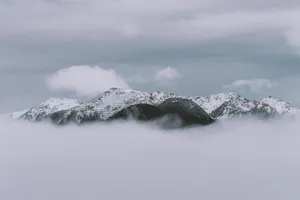 A serene winter view of snow-capped mountains rising above misty clouds on a cloudy day. jigsaw puzzle