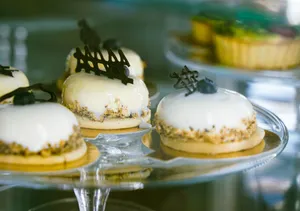 Close-up of gourmet pastries with white glaze and chocolate decor on a glass stand. jigsaw puzzle
