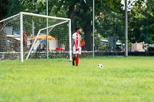 Soccer goalkeeper in action on outdoor field. Player in red kit ready near goal. jigsaw puzzle