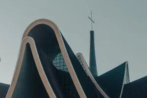 Low angle view of a modern catholic church with a wavy roof and cross, under clear sky. jigsaw puzzle