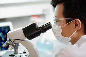 Scientist wearing face mask and goggles examining samples through a microscope in a lab. jigsaw puzzle