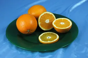 Close-up of whole and sliced oranges on a green plate against a blue background. jigsaw puzzle
