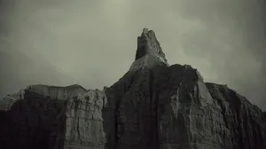 A dark, jagged mountain peak under a cloudy sky. jigsaw puzzle