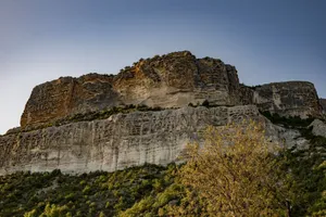 Stunning view of a rocky cliff surrounded by greenery under a clear blue sky, showcasing nature's beauty. jigsaw puzzle