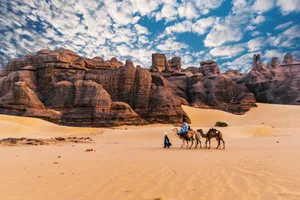 Scenic view of camels and sandstone cliffs in Tamanrasset, Algeria under a vibrant sky. jigsaw puzzle