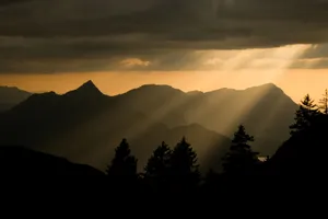 A breathtaking view of sun rays piercing through clouds over a mountain range at sunset. jigsaw puzzle