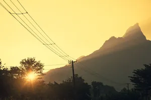 Serene sunset with mountain silhouette and power lines, offering a warm and tranquil landscape. jigsaw puzzle