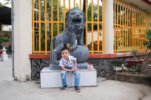 Young boy sitting on a bench beside a lion statue in an outdoor area in Ho Chi Minh City, Vietnam. jigsaw puzzle