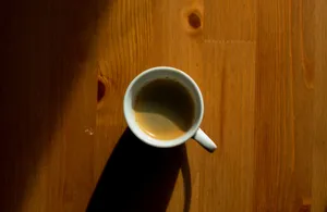 A simple, minimalist approach capturing a cup of coffee casting a shadow on a wooden table. jigsaw puzzle
