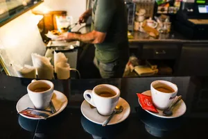 A barista in a café preparing espresso drinks on a countertop with three coffee cups in focus. jigsaw puzzle