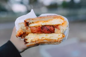 Close-up of a delicious breakfast sandwich with cheese and bacon held outside. jigsaw puzzle