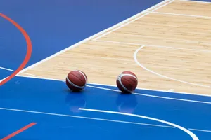Two basketballs resting on a blue indoor basketball court with wooden flooring. jigsaw puzzle