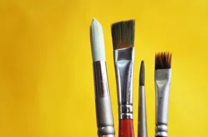 Close-up of varied paint brushes against a bright yellow backdrop. jigsaw puzzle