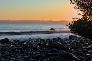 the sun is setting over the ocean with rocks on the shore jigsaw puzzle