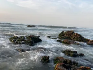 Ocean waves crash over dark rocks under a hazy sky. jigsaw puzzle