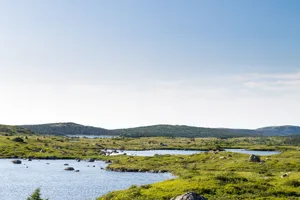 Scenery of rippling lake with grassy shore and boulders surrounded by hills under blue sky jigsaw puzzle