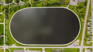 Drone view of black oval reservoir in park surrounded by greenery and settlement in daylight jigsaw puzzle