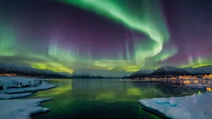 Vibrant northern lights illuminate a serene snow-covered landscape with icy waters. jigsaw puzzle
