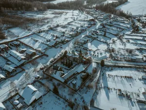 Aerial shot of a snow-covered rural village with scattered houses and a church surrounded by snowy fields. jigsaw puzzle