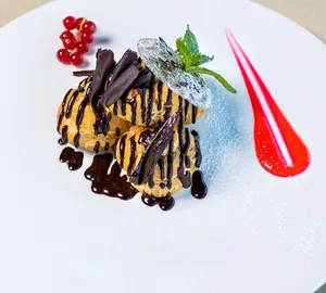 Sumptuous profiteroles topped with chocolate sauce and berries, presented on a white dish. jigsaw puzzle