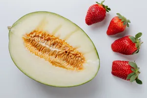 A close-up of a halved melon and fresh strawberries on a white background. jigsaw puzzle