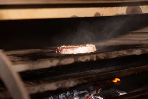 Close-up of a delicious steak cooking on a grill over an open flame, emitting smoke. jigsaw puzzle
