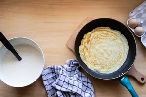 Top view of a pancake cooking in a pan with batter and eggs nearby. jigsaw puzzle