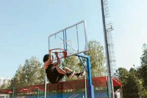 Man hanging on a basketball hoop after an impressive dunk on an outdoor court. jigsaw puzzle