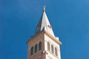 Close-up of a historic church steeple with a cross against a bright blue sky, showcasing religious architecture. jigsaw puzzle