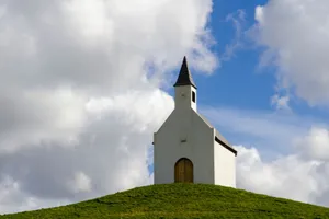 A serene chapel perched on a grassy hilltop under a dramatic cloudy sky, capturing the essence of rural tranquility. jigsaw puzzle