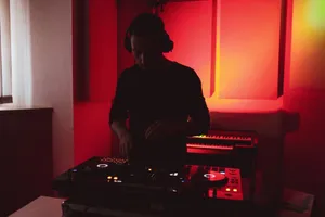A DJ wearing headphones mixes music on a console in a dimly lit studio with red lighting. jigsaw puzzle
