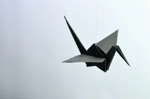 A minimalist black origami crane elegantly suspended against a soft background. jigsaw puzzle