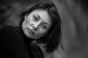Black and white portrait capturing the intense gaze of a woman in a serene outdoor setting. jigsaw puzzle