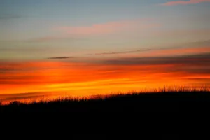 A vibrant sunset with fiery orange and red hues over a silhouetted landscape. jigsaw puzzle