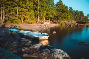 A serene lakeside view with a small boat resting on rocks, surrounded by lush trees at sunset. jigsaw puzzle