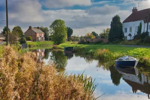 a small boat floating on top of a river next to a lush green field jigsaw puzzle