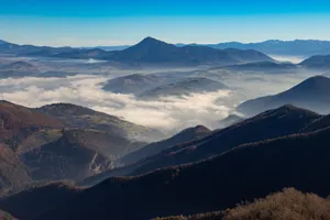 A breathtaking view of mountain ranges blanketed by clouds under a clear blue sky. jigsaw puzzle